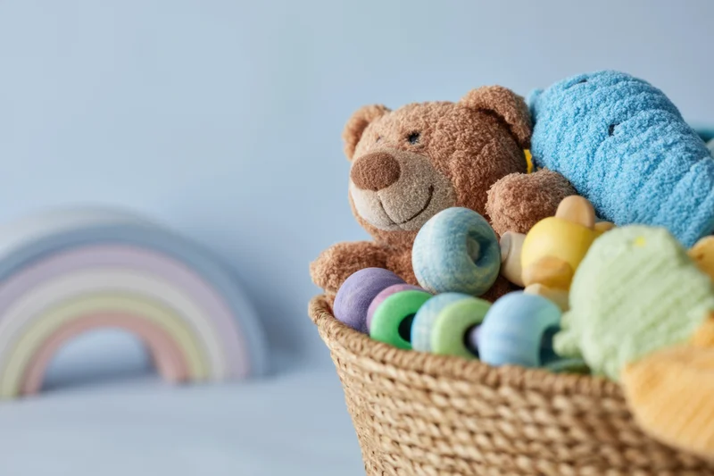 Woven basket filled with plush toys and wooden rings in a pastel nursery setting
