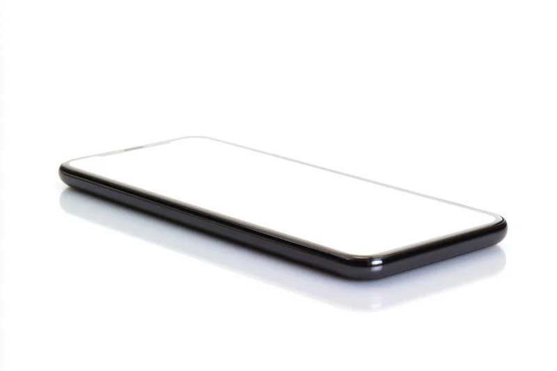 Sleek smartphone with blank white screen lying flat on white surface