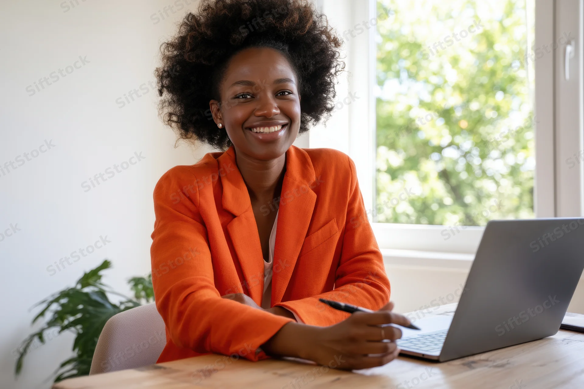 Smiling woman in orange jacket sitting at desk with laptop in office setting