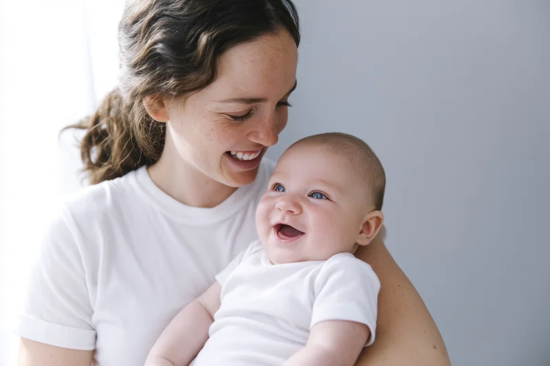 Young woman smiling while holding a laughing baby in her arms indoors