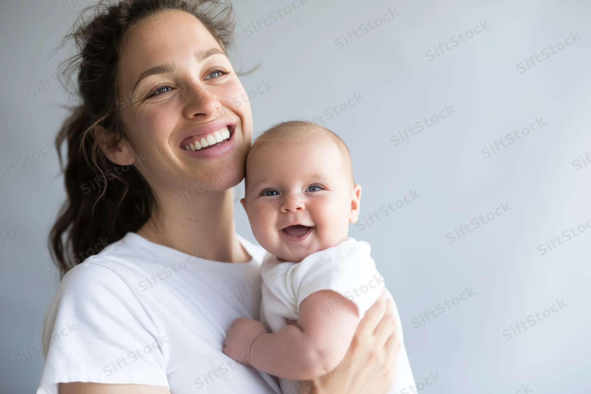Young woman smiling while holding a happy baby close to her chest indoors
