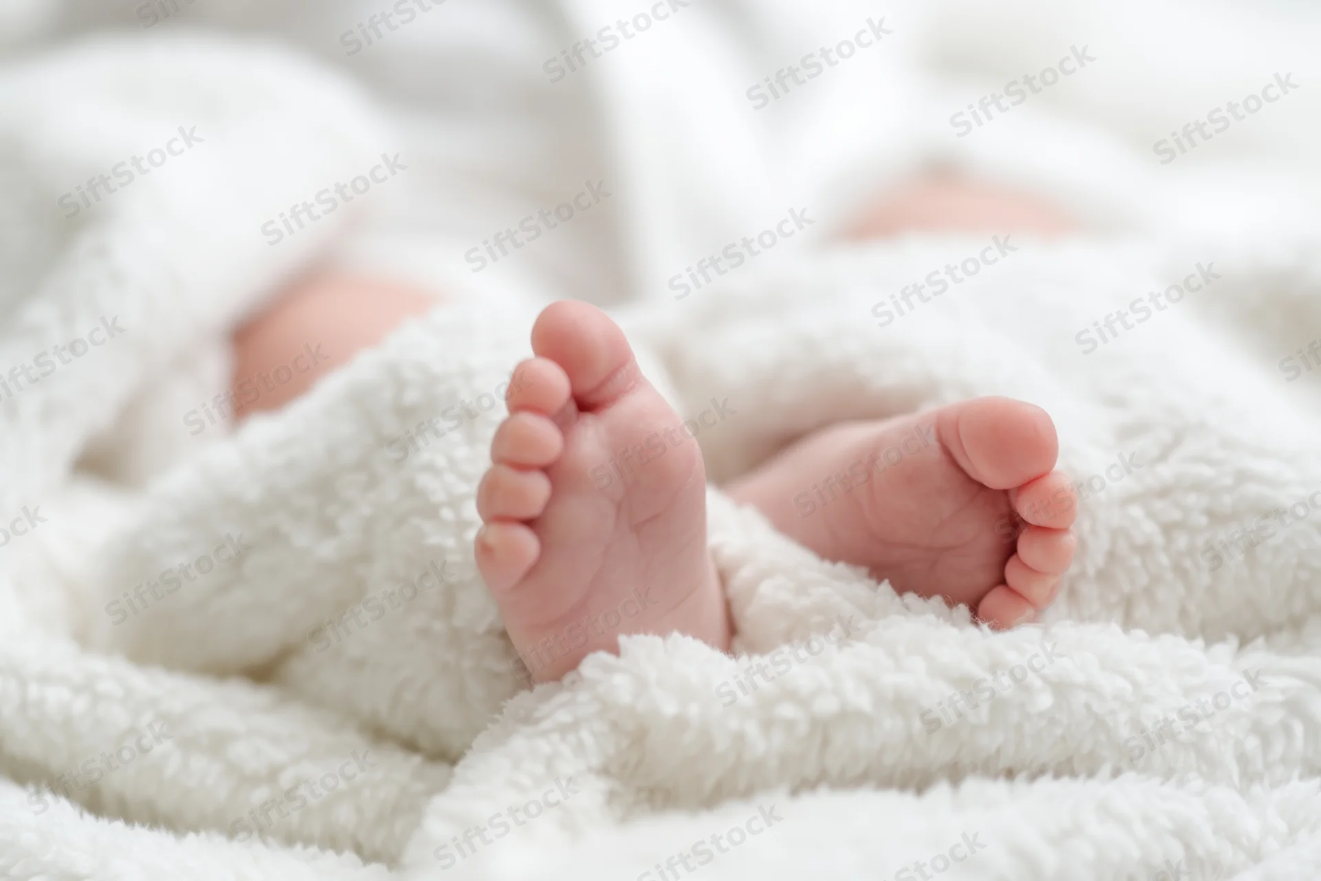 Close-up of a baby's tiny feet resting on a fluffy white blanket