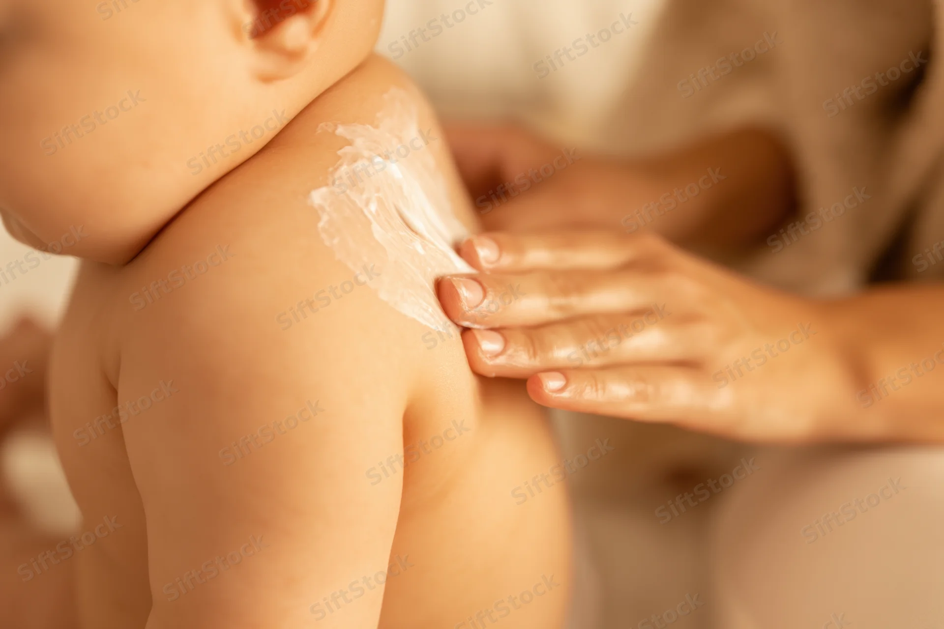 Baby receiving lotion application on back by mother's hand