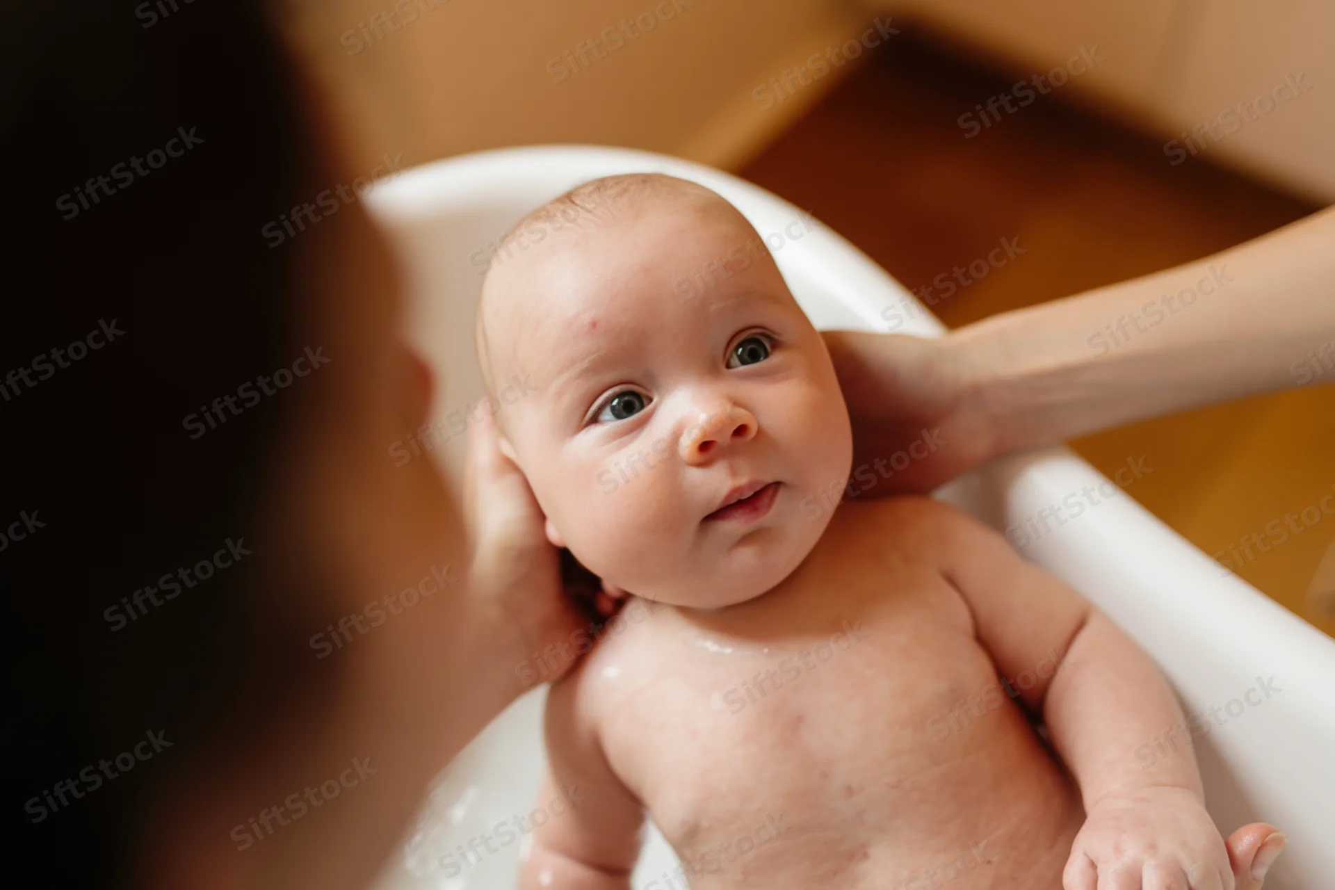 Baby being bathed in white tub with adult hands supporting head and body