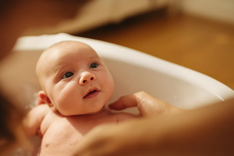 Newborn baby being gently supported in a white bathtub during bath time