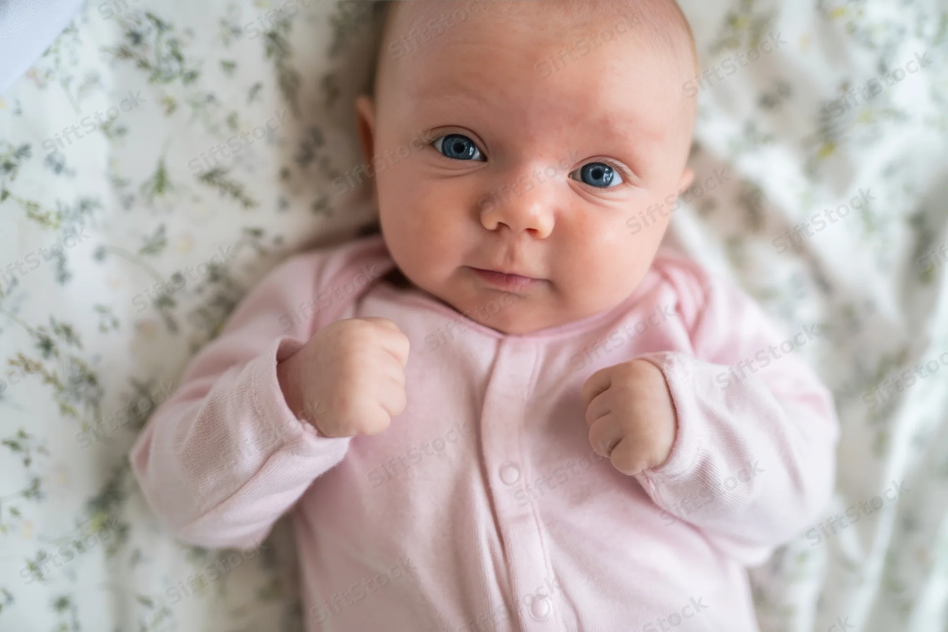 Baby lying on floral sheet wearing pink onesie
