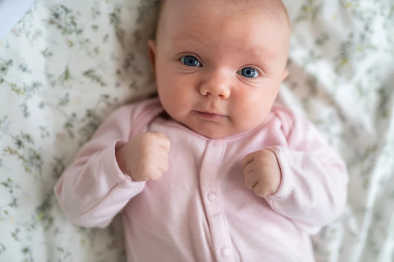 Baby lying on floral sheet wearing pink onesie