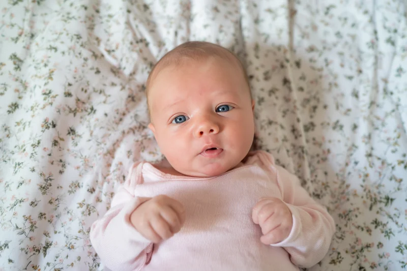 Baby lying on floral sheet wearing pink onesie