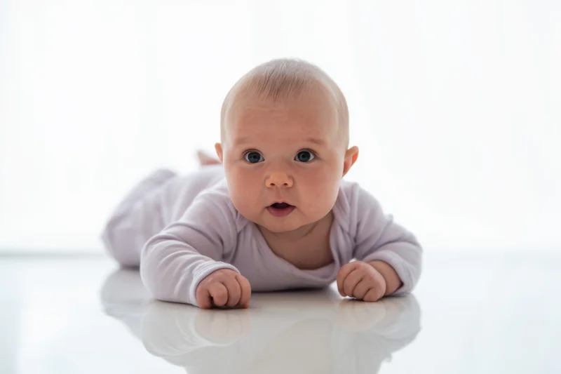 Baby lying prone on glossy white surface propped on forearms