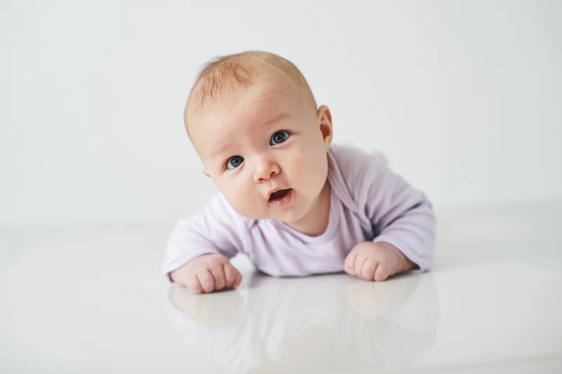 Baby lying on glossy white surface propped on forearms with reflection visible