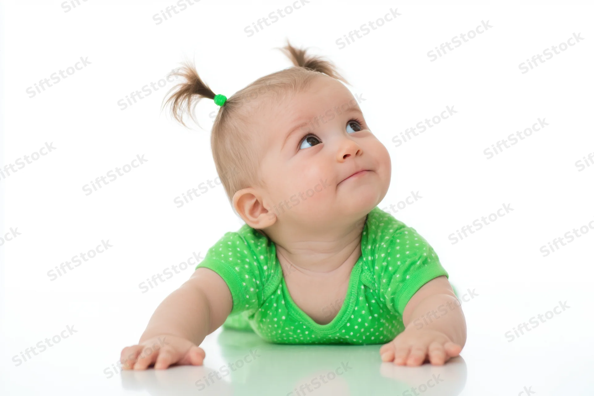 Baby lying on stomach on white studio background with pigtails and green polka dot onesie