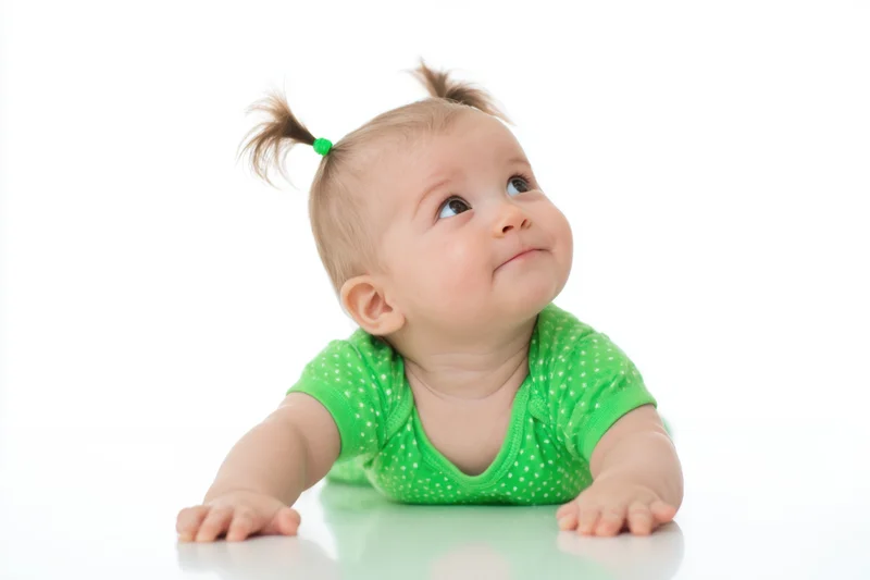 Baby lying on stomach on white studio background with pigtails and green polka dot onesie