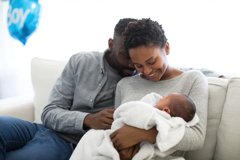 Couple cradling newborn baby on light sofa in bright living room