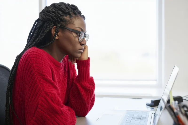Focused woman with box braids and glasses working on laptop at office desk