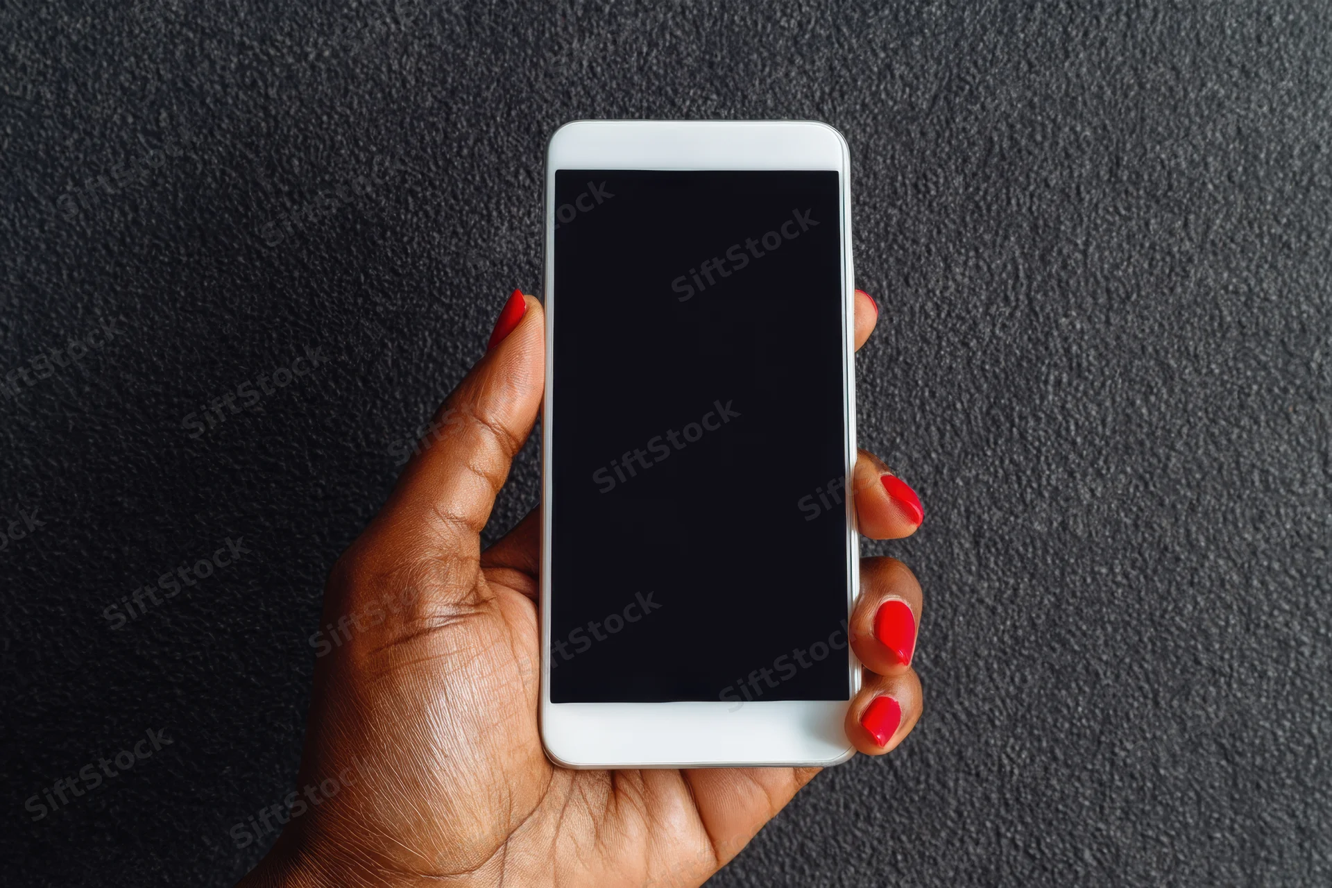 Woman's hand with red nail polish gripping a white smartphone with blank screen against dark textured background