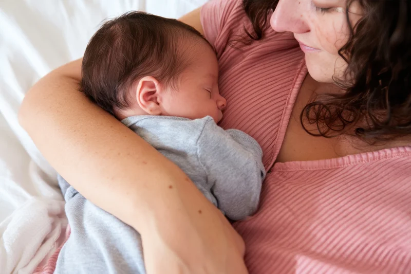 Mother cradling sleeping newborn against her chest in bed