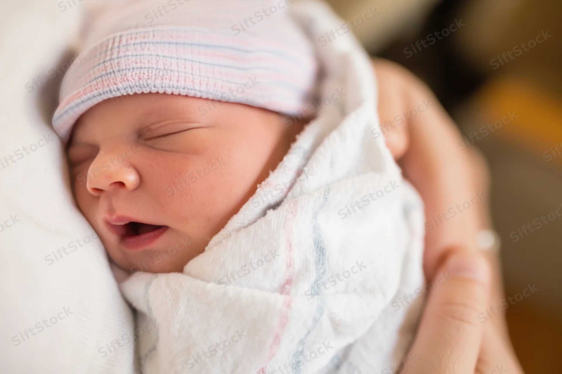 Newborn baby sleeping swaddled in white blanket held gently in hands