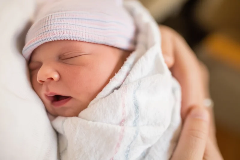 Newborn baby sleeping swaddled in white blanket held gently in hands