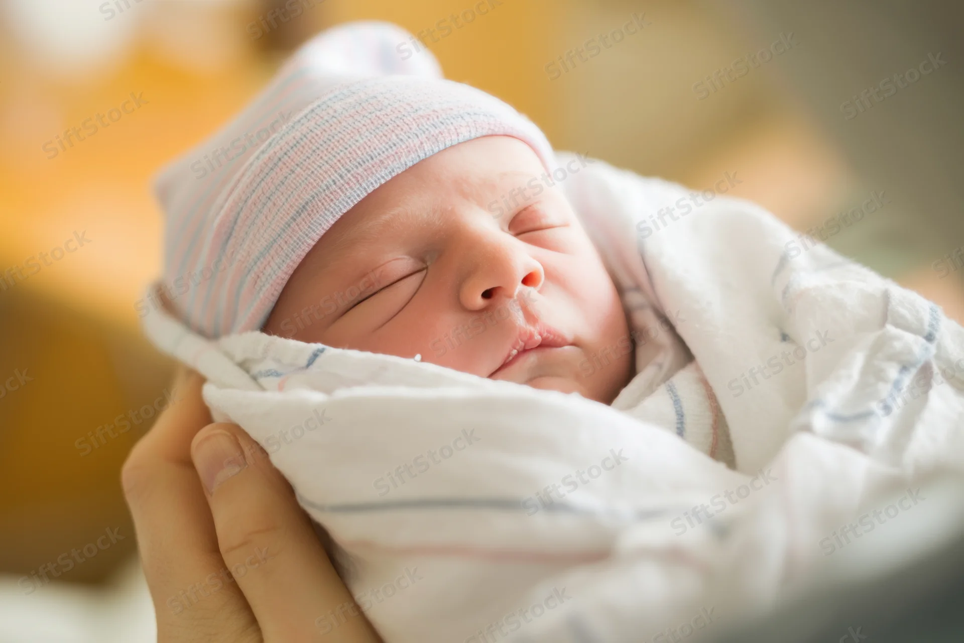 Newborn baby sleeping swaddled in white blanket held gently in hands