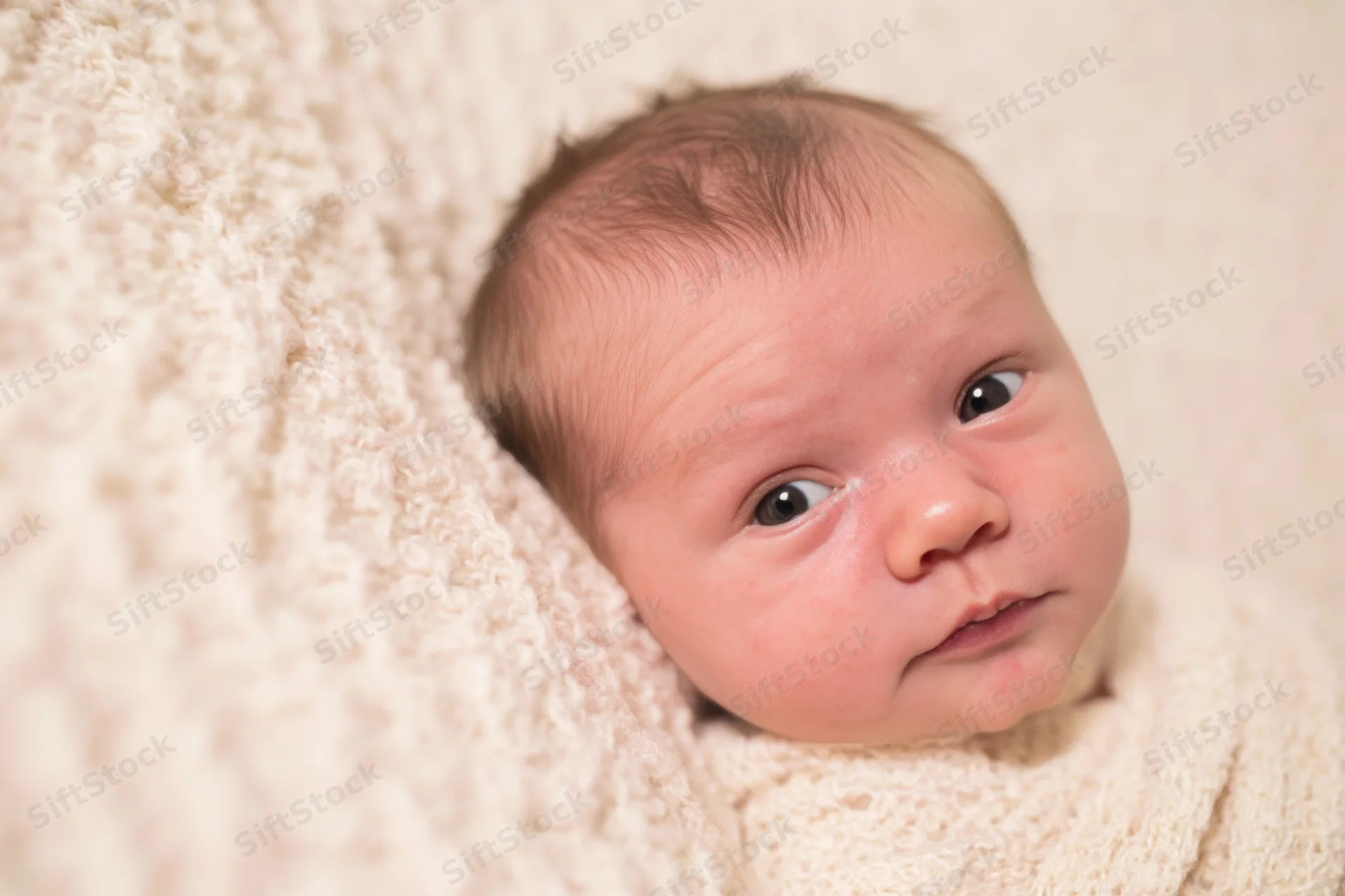 Newborn baby lying on soft cream blanket wide awake with alert eyes