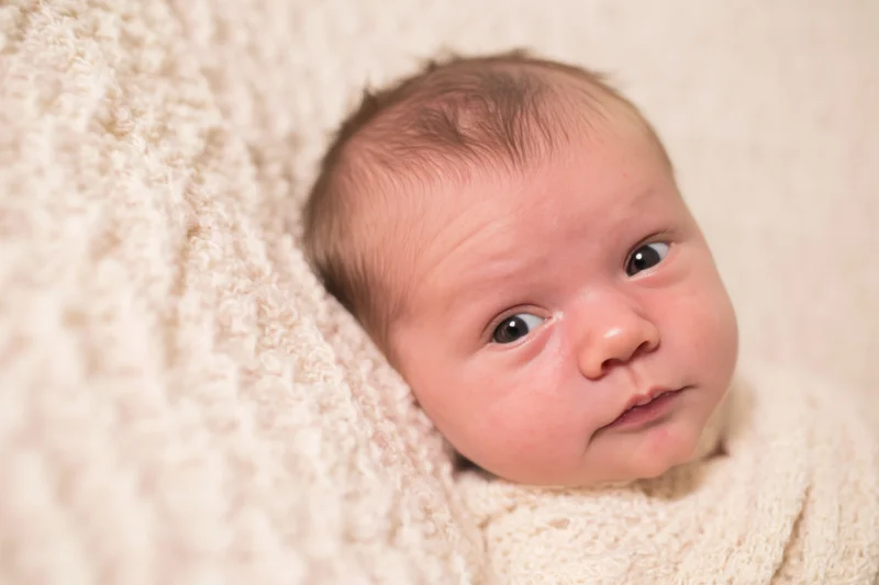 Newborn baby lying on soft cream blanket wide awake with alert eyes
