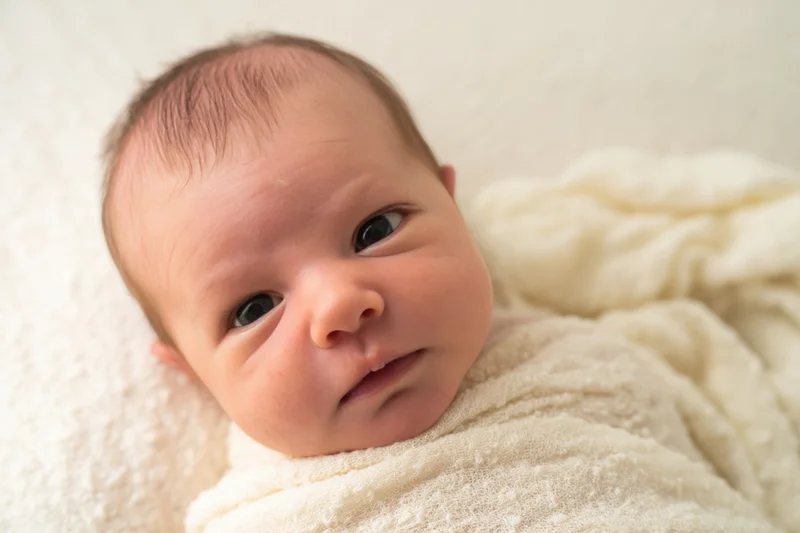 Newborn baby lying awake on a soft cream blanket wrapped in a white swaddle