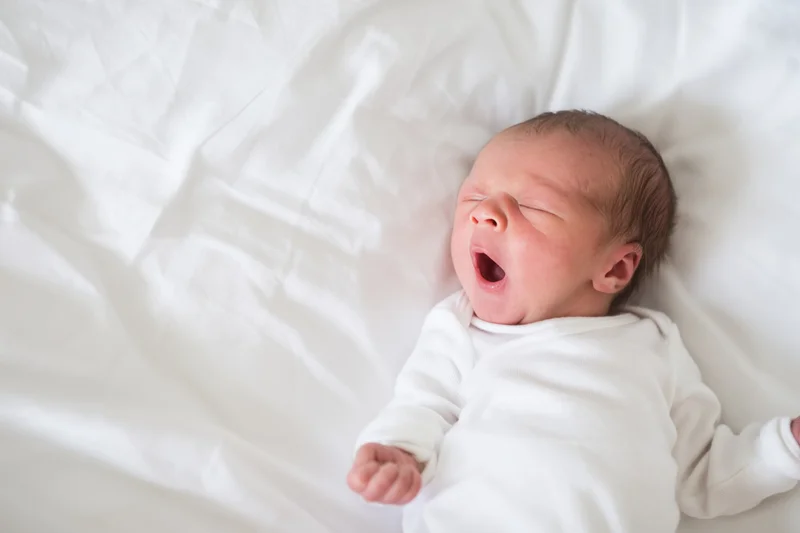 Newborn baby yawning while lying on a white bed blanket