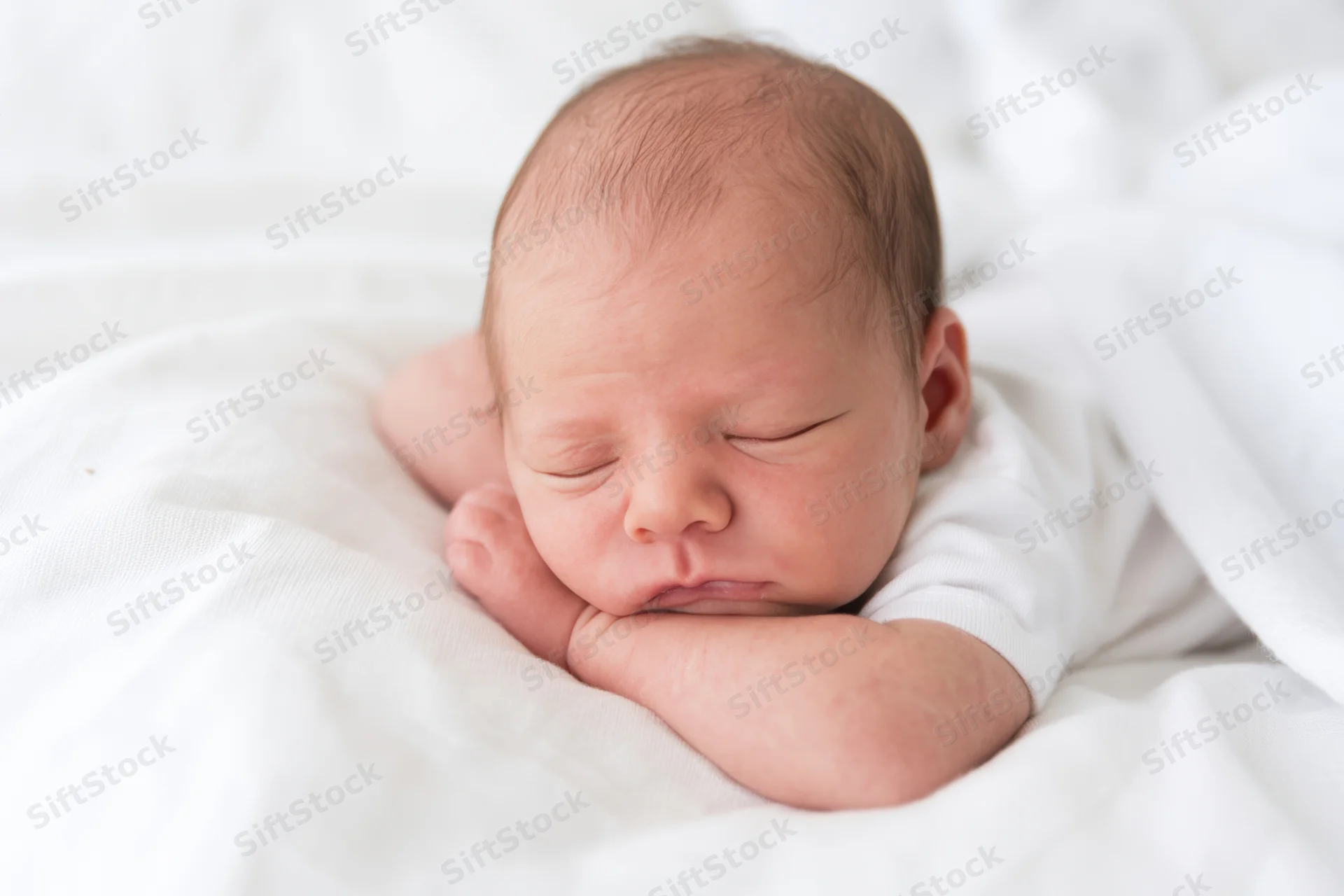 Newborn baby sleeping with arms curled under chin on white blanket