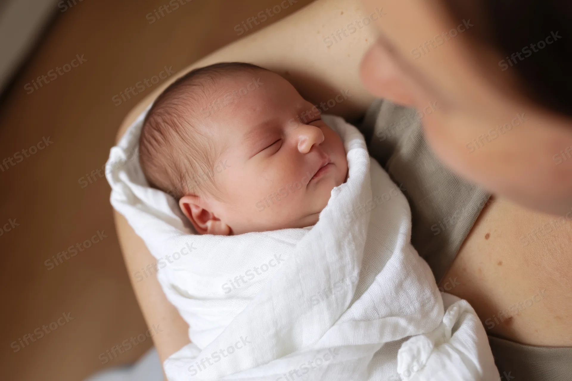 Newborn baby wrapped in white blanket cradled in mother's arms