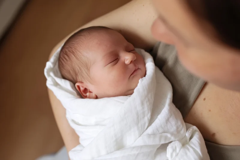 Newborn baby wrapped in white blanket cradled in mother's arms