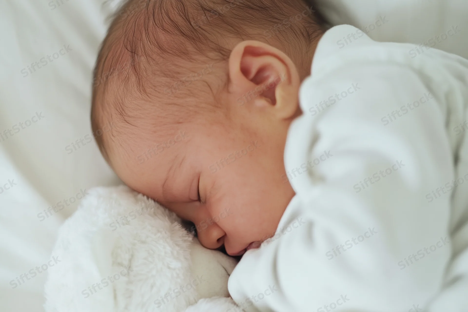 Sleeping baby cuddling a white plush bear in a soft bed