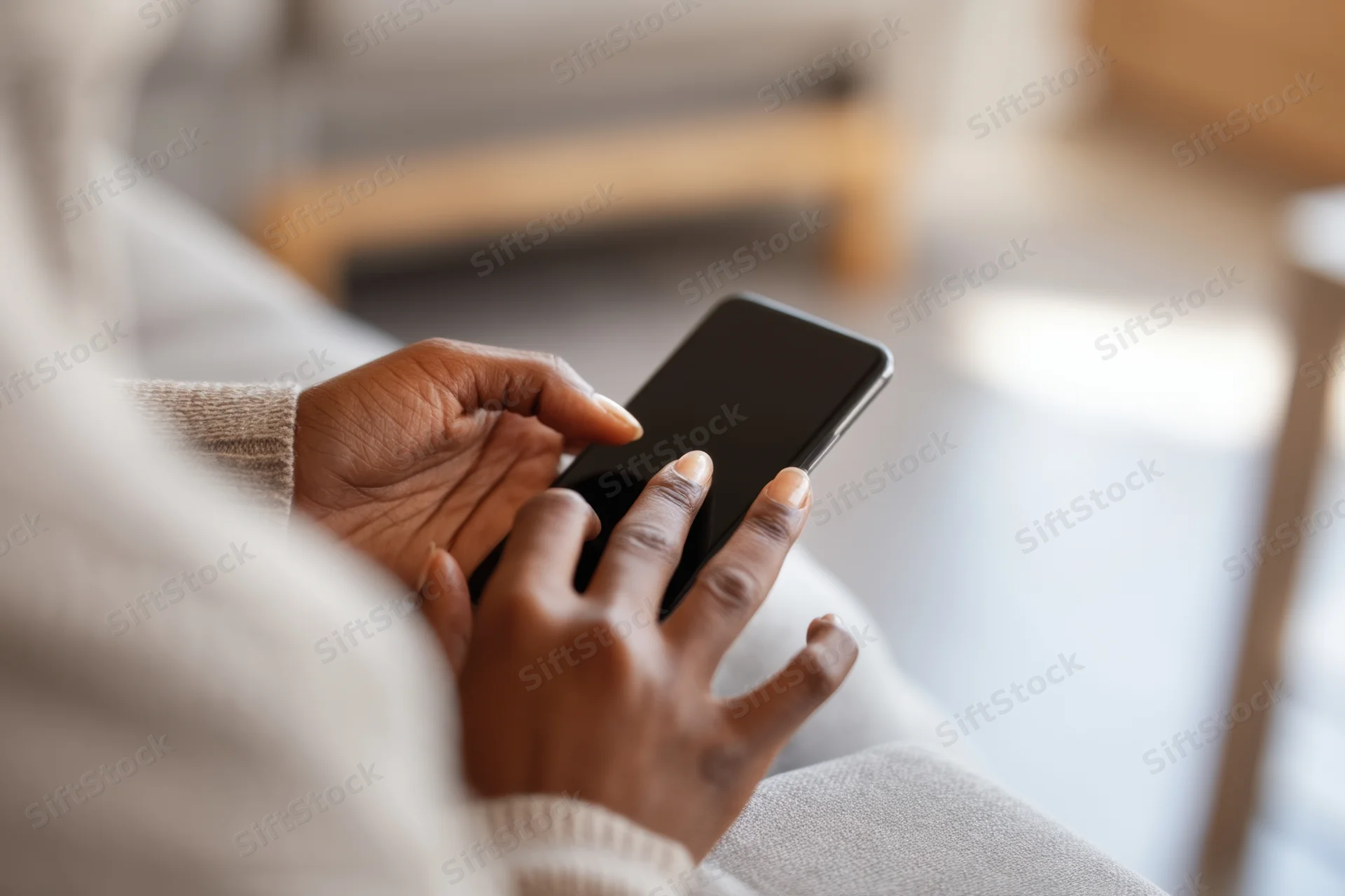 Closeup of a woman’s hands using a smartphone while sitting on a couch indoors
