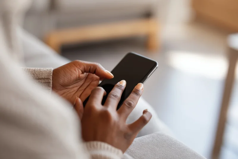 Closeup of a woman’s hands using a smartphone while sitting on a couch indoors