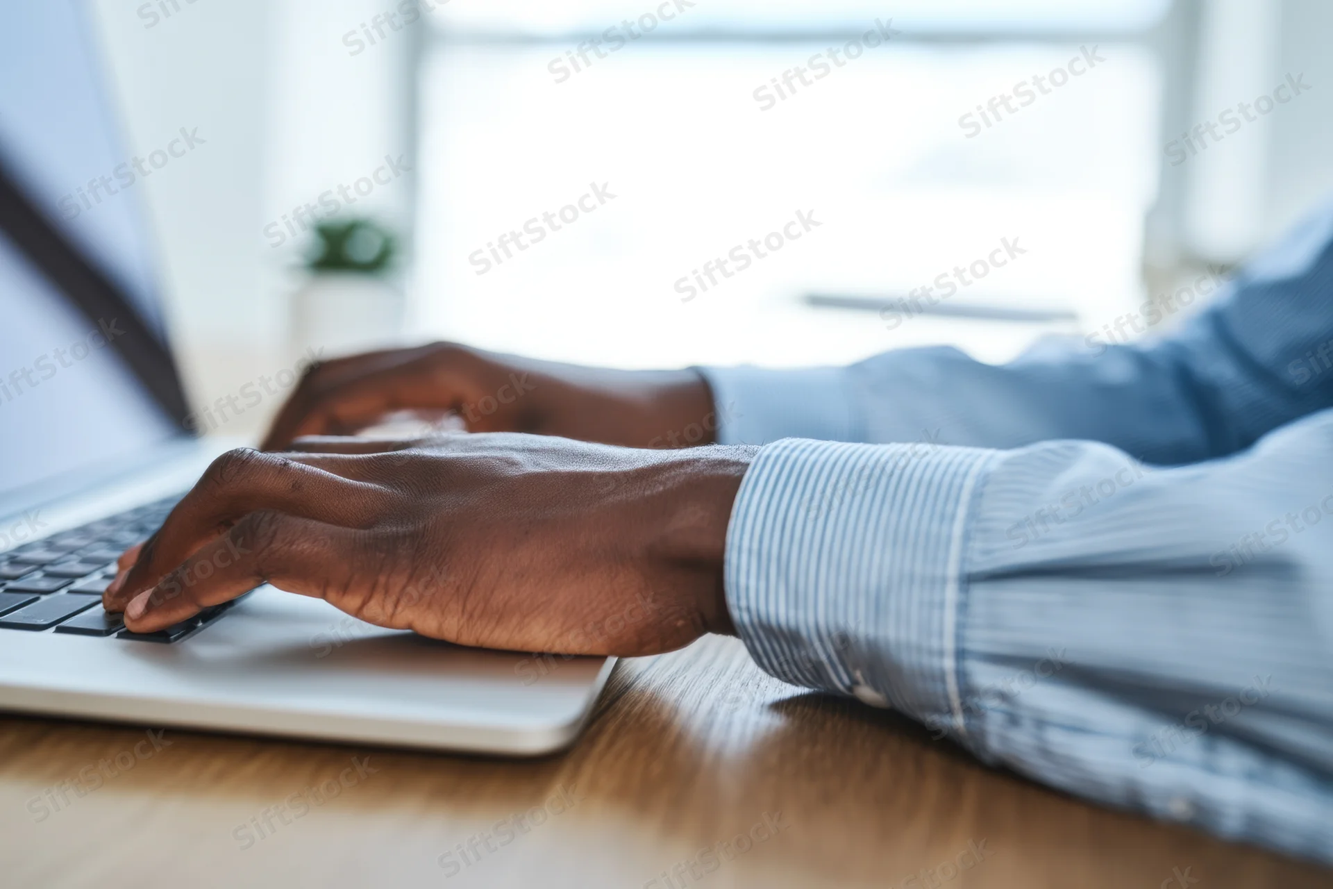 Hands typing on a silver laptop at a wooden desk in an office setting