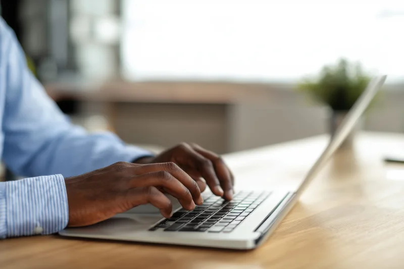 Man typing on silver laptop at wooden desk in office setting