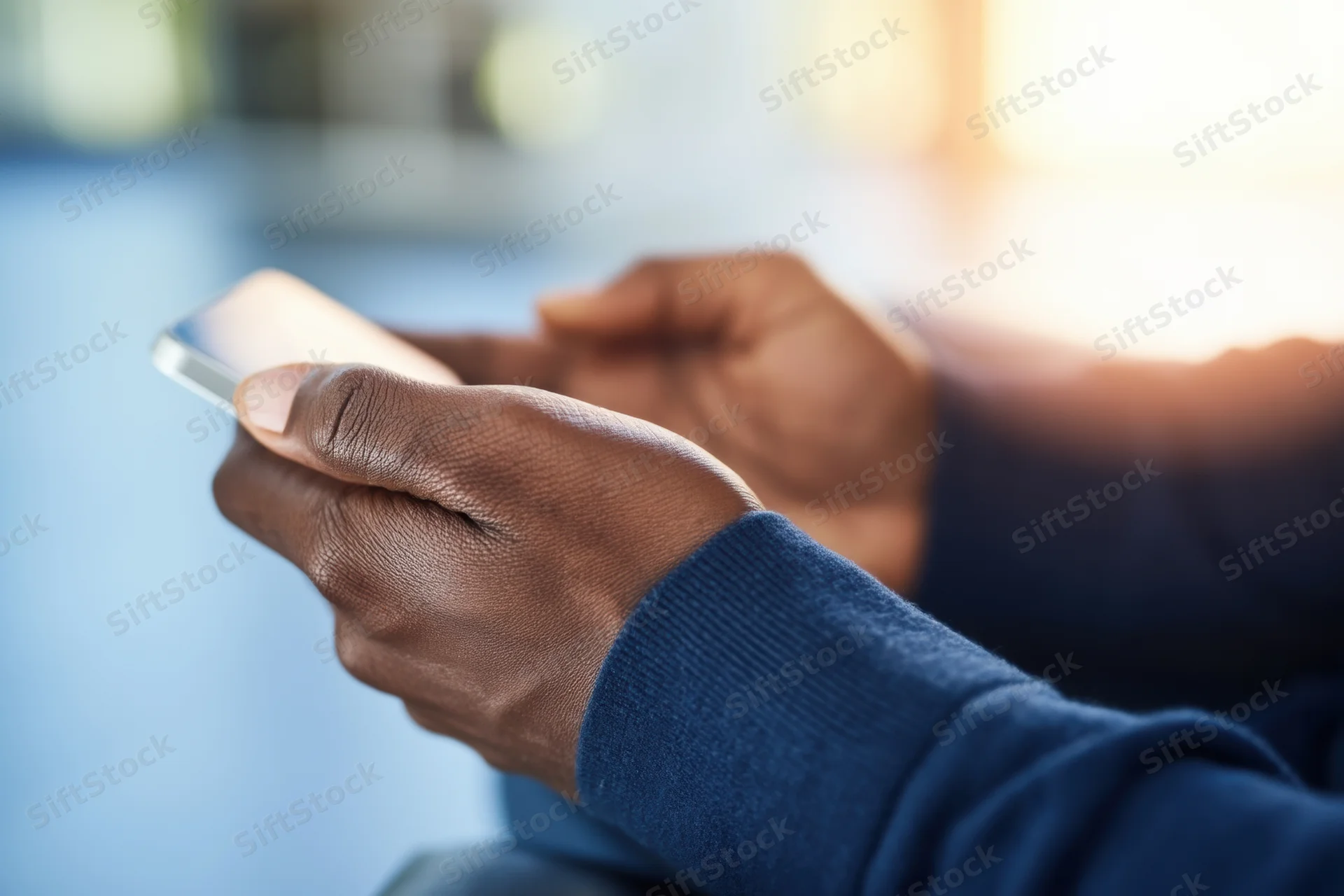 Hands holding a smartphone while texting in an indoor setting with blurred background