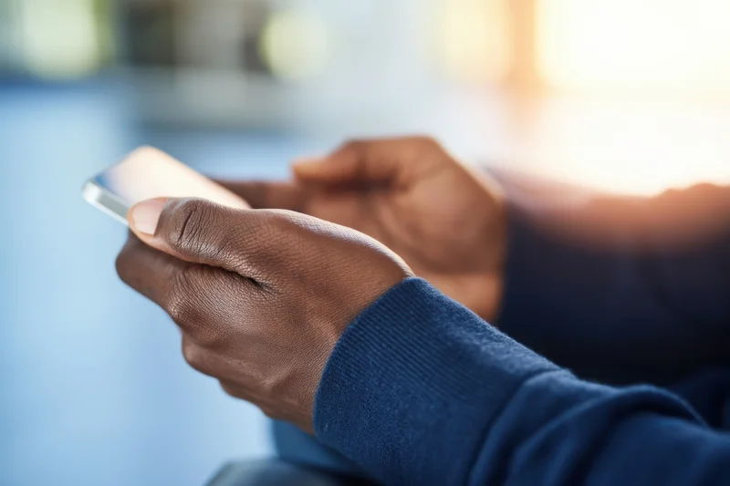 Hands holding a smartphone while texting in an indoor setting with blurred background