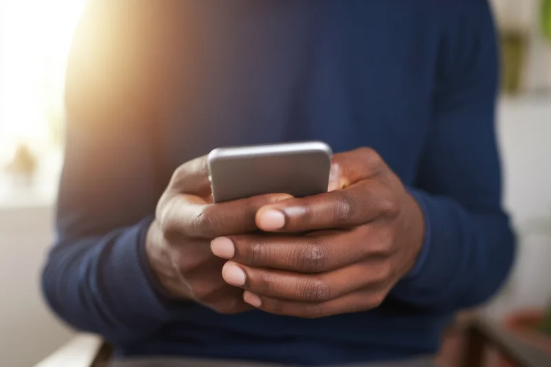 Man cradling smartphone with both hands while seated indoors