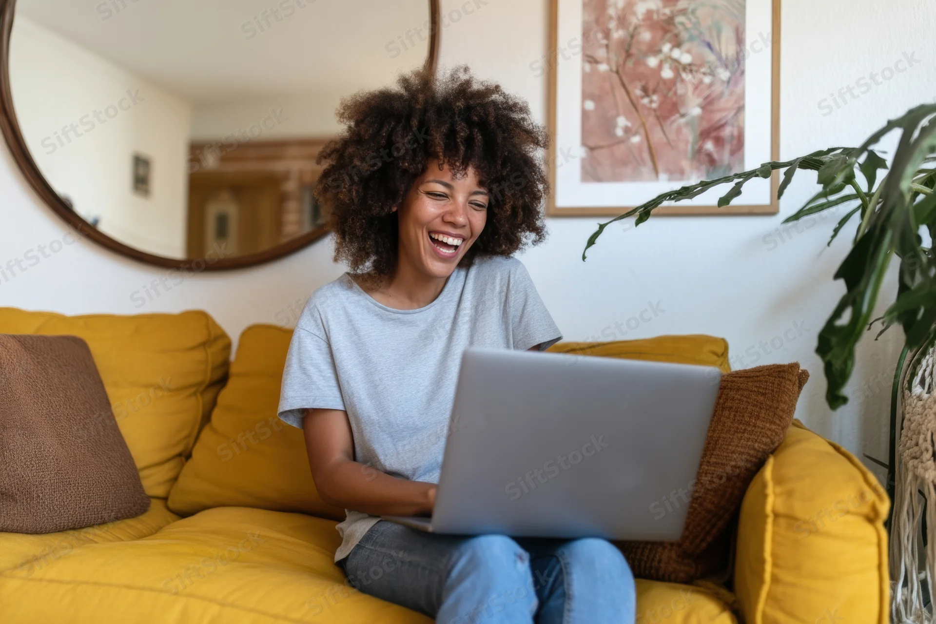 Woman laughing while using laptop on yellow sofa in living room