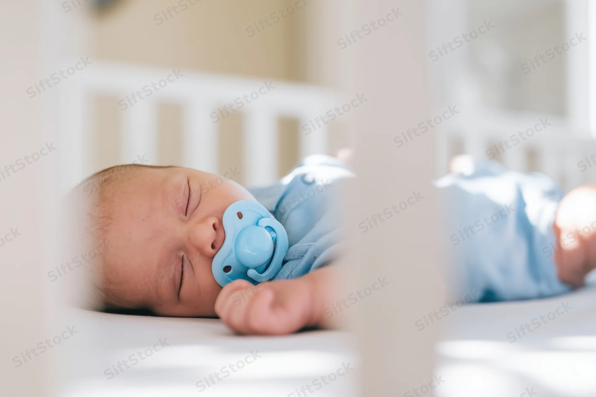 Sleeping newborn in white crib with blue pacifier and light blue outfit