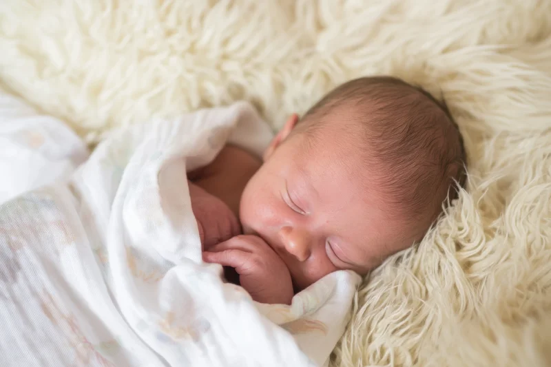Newborn baby sleeping swaddled in a white blanket on a fluffy ivory fur surface