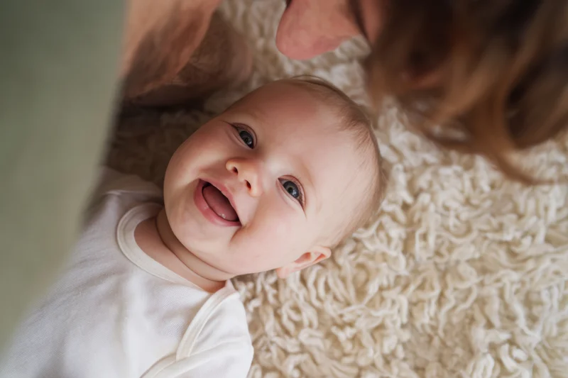 Smiling baby lying on soft shaggy rug with adult leaning over