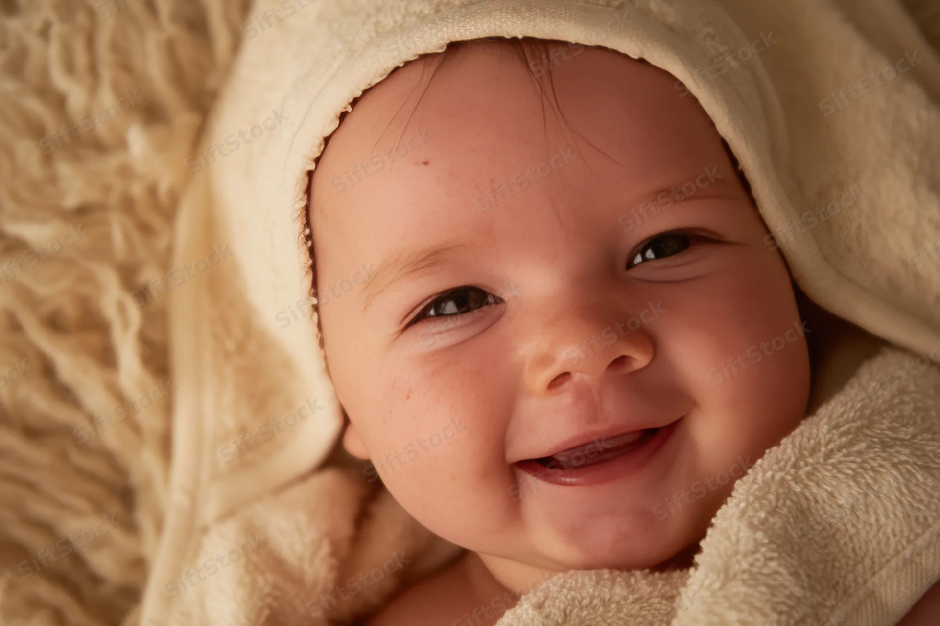 Smiling baby nestled in a soft cream towel under warm light