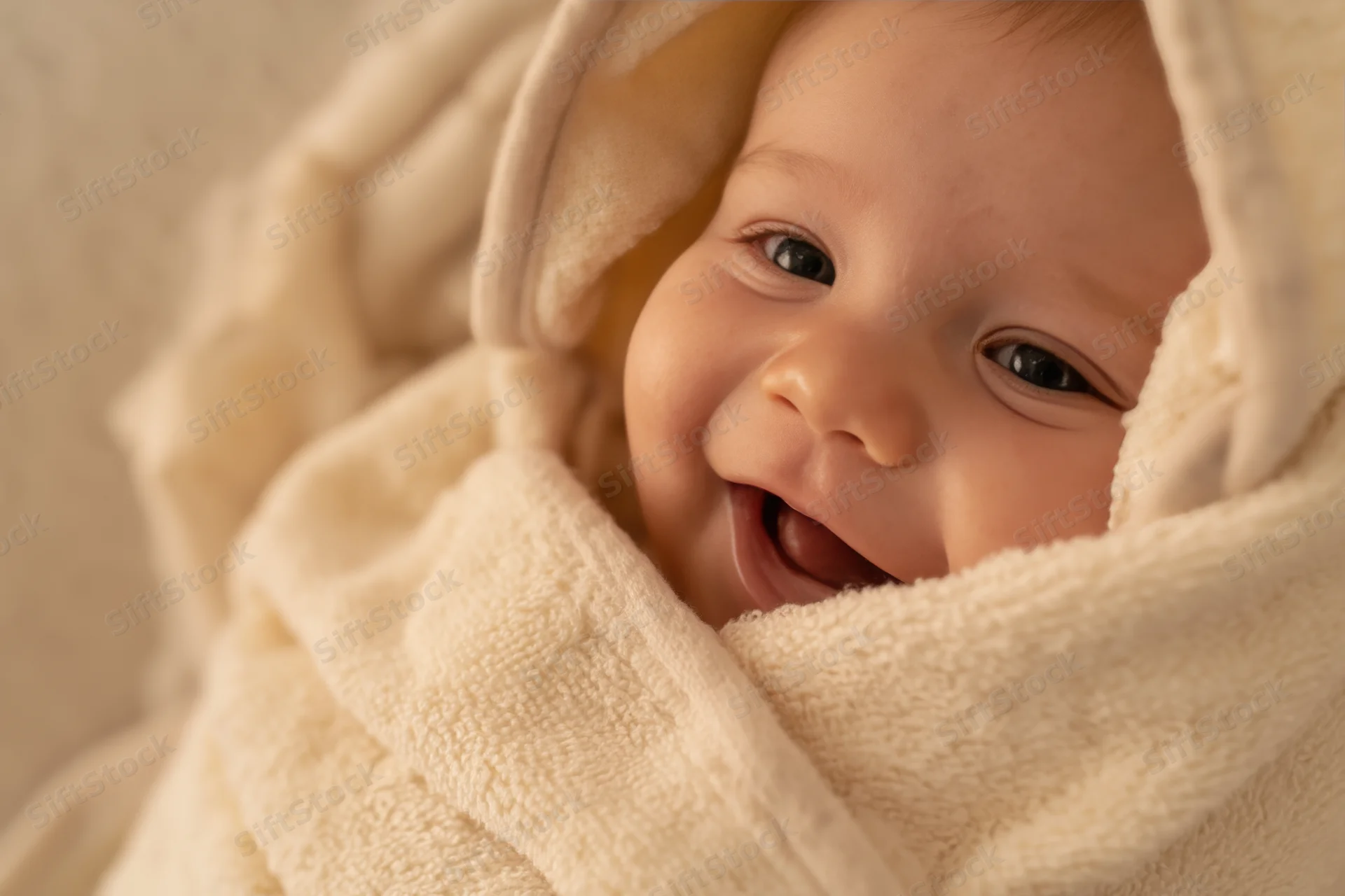 Smiling baby wrapped in a soft cream towel with warm light