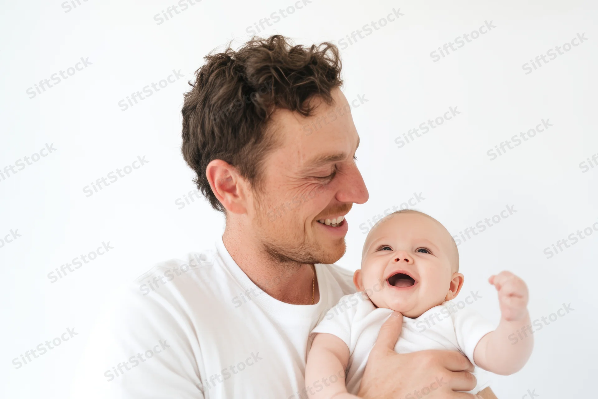 Father holding laughing baby in white t-shirt, smiling at child in studio setting