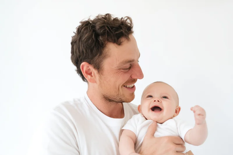 Father holding laughing baby in white t-shirt, smiling at child in studio setting