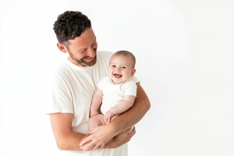 Father holding laughing baby in white t-shirt against white background