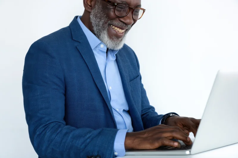 Smiling man in blue blazer typing on laptop at white desk
