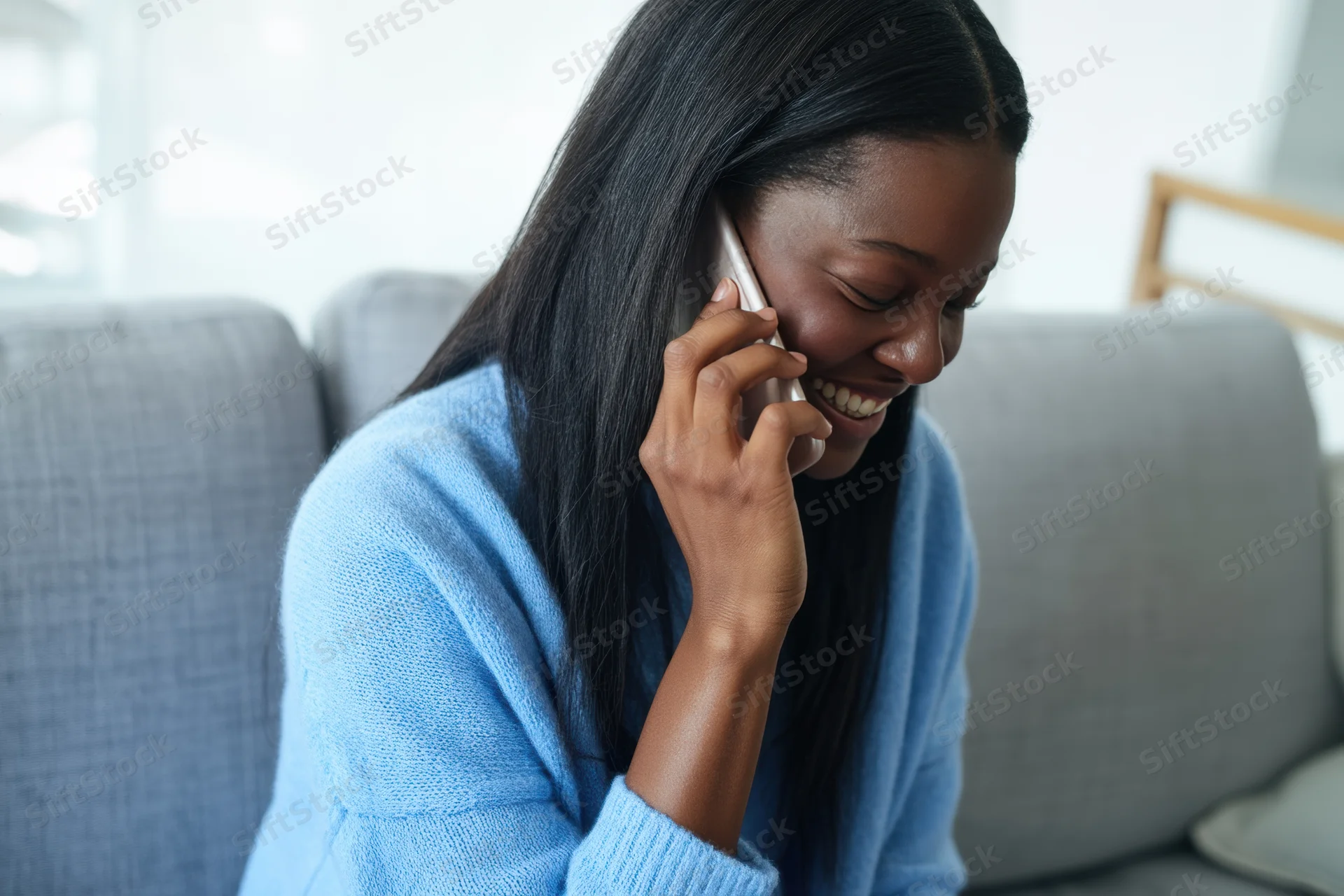 Woman laughing while talking on smartphone seated on sofa in living room