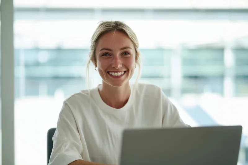 Young woman smiling at camera while sitting at desk with laptop in office setting